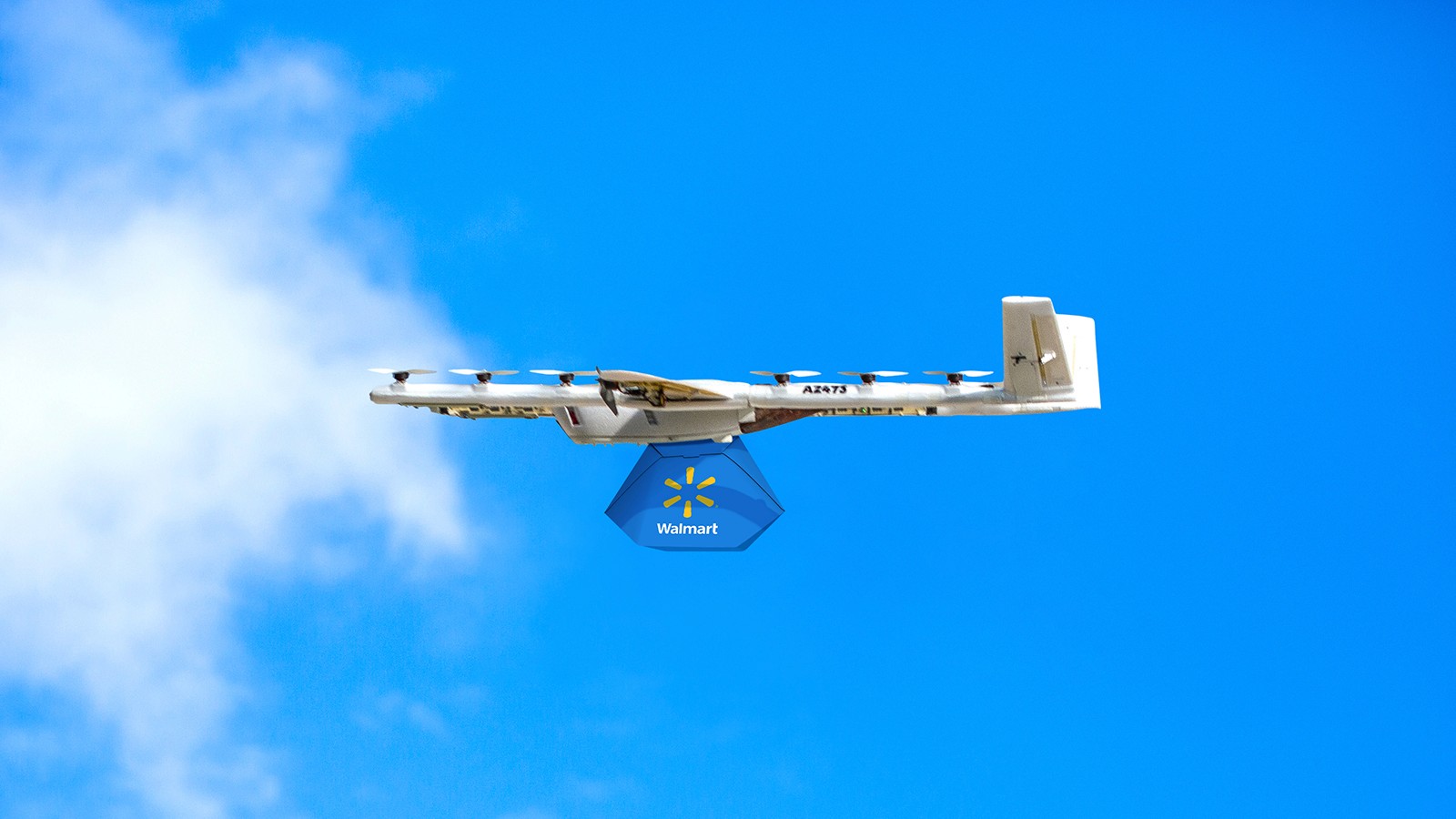 A white and yellow drone in flight against a clear blue sky; it is carrying a walmart package, demonstrating modern delivery technology.